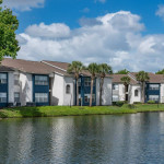 View of apartments by the lake at Solis At Winter Park, featuring lush greenery and blue skies.