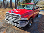 1998 Dodge Ram 1500 V6 in red with 143,698 miles and new headlights parked in a wooded area.