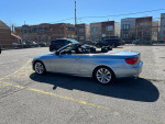 2000 BMW 3 Series 328i convertible parked with a clear blue sky and city buildings in the background