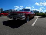 1997 Cadillac DeVille in candy apple red parked, showcasing chrome Dayton wire wheels and a clean exterior.