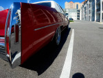 1997 Cadillac DeVille in candy apple red, showcasing chrome spokes and sleek design parked in a lot.