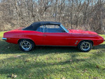 1969 Pontiac Firebird convertible parked on grass, featuring red paint and black soft top.
