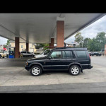Black 2004 Land Rover Discovery 2 parked at a gas station, with nearby vehicles visible.