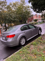 2010 Subaru Legacy parked on a street, featuring a silver exterior and surrounded by greenery.