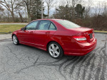 2010 Mercedes-Benz C300 Sport in red, showcasing sleek design and AWD capabilities on a scenic roadway.