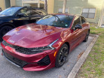 Red 2023 Kia K5 GT with sleek design, parked beside another vehicle, showcasing modern styling.
