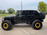 Side view of a 2016 Jeep Rubicon Hard Rock with black body and yellow accents parked outdoors