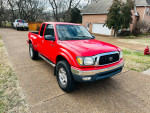 2003 Toyota Tacoma V6 in red parked on a driveway, showcasing its clean exterior and wheels.