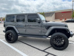 Customized 2019 Jeep Wrangler Unlimited Sahara with black rims and large tires parked in a lot.