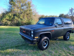 1987 GMC Jimmy Sierra Classic with satin black paint parked in grassy area, showcasing its rust-free condition and new tires.