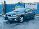 2013 Honda Civic Hybrid in gray, showcasing alloy wheels and rear camera, parked in front of marina entrance.