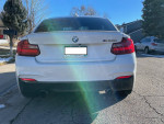 Rear view of a white 2015 BMW m235i coupe with custom exhaust parked on a sunny street.