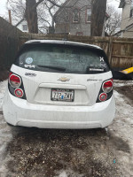2016 Chevrolet Sonic LT in white with black rims parked in a snowy area, showcasing stylish design and accessories.