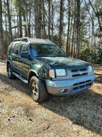 2000 Nissan Xterra SE RWD in green, parked in a wooded area, showing minor front damage.