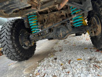 Undercarriage view of a modified Toyota Tacoma with suspension and wheel details on gravel surface.