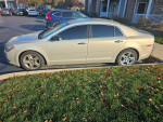 2010 Chevrolet Malibu with 64,000 miles parked beside a grassy area and autumn leaves.
