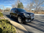 2016 GMC Acadia Denali in black parked on a sunny day, featuring alloy wheels and winter-ready tires.