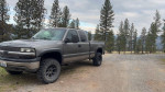 2000 Chevrolet Silverado 1500 4x4 on a gravel road surrounded by trees, showcasing its rugged design and aftermarket upgrades.