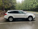 2011 Subaru Outback 2.5i AWD parked on a road surrounded by lush greenery, showcasing its sleek design and immaculate condition.