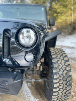 Close-up of a black 2009 Jeep Wrangler Rubicon showcasing the front fender and off-road tire on a snowy path.