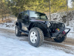 2009 Jeep Wrangler Rubicon 4WD parked on snowy road, featuring new bumper and winch, clean condition with rebuilt title.