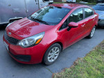 2013 Kia Rio in red, featuring power steering and automatic transmission, parked on a driveway.
