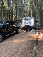 2012 Ford F350 diesel truck parked next to a camper in a forest campsite with solar panels.