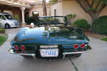 Back view of a restored 1967 Chevrolet Corvette convertible in green, parked with a home in the background.