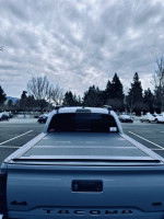 Rear view of a 2021 Toyota Tacoma SR5 4WD parked, showcasing the cement color and truck bed.