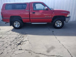 1995 Dodge Ram 1500 SLT V8 4x4 in red parked on cracked pavement, showcasing its clean condition and rugged tires.