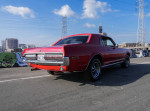 Classic 1968 Mercury Cougar in a vibrant red color parked on the street with city skyline in the background.