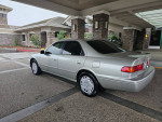 2000 Toyota Camry LE in silver, low mileage, parked in a driveway with lovely stonework in background.