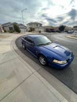 2004 Ford Mustang in blue parked on the street, showing good condition and minor exterior imperfections.