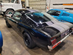 1965 Ford Mustang 2+2 Fastback in Raven Black with charcoal stripes, showcasing its classic design and sleek profile.