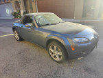 2007 Mazda MX-5 Sport with 98,000 miles parked in a driveway, showcasing its blue exterior and sleek design.