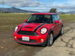 2010 Mini Cooper S in red with black stripes parked on a rural road, showcasing its clean and well-maintained exterior.