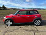Side view of a well-maintained 2010 Mini Cooper S in red, parked in an open field.