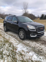 2014 GMC Acadia in black, all-wheel drive, parked on snowy gravel with trees in background.