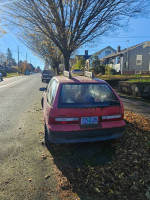 1990 Geo Metro parked on the street with autumn leaves, showing salvage title and visible wear.