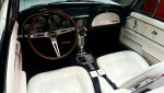 Interior view of a 1965 Chevrolet Corvette Convertible with white leather seats and classic dashboard.