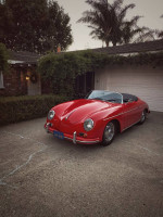 Red Porsche 365 Speedster convertible parked in a driveway, showcasing classic design and pristine condition.