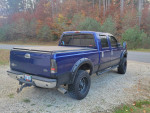 Blue 2004 Ford F350 King Ranch truck with aftermarket wheels parked on gravel road